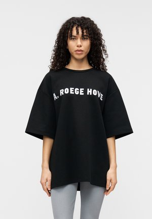 T-shirt noir oversize en coton, avec des manches courtes et un col rond. "A. ROEGE HOVE" est imprimé en blanc sur la poitrine.