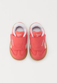 Bottes de sport rouges avec une sangle en velcro, des accents blancs, un intérieur rembourré et une semelle en caoutchouc brun flexible. Convient aux jeunes enfants.