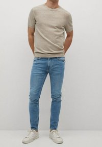 Camiseta beige de manga corta hecha de un material suave, combinada con jeans ajustados de color azul claro y zapatillas blancas con una superficie texturizada.
