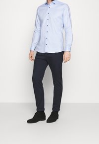 Light blue long-sleeve shirt with dark buttons, paired with dark slim-fit pants and black suede shoes. Smooth fabric, classic collar design.