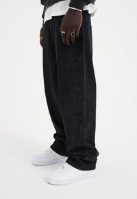 Svartmönstrade vida jeans med fickor i synlig stil. Matchas med vita sneakers. Har en subtil textur på tyget.