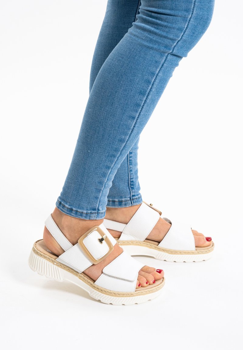 Sandalias blancas con suela gruesa y una correa ancha que presenta una hebilla cuadrada. Material texturizado y un detalle de corte similar al yute.