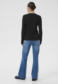 Sort tekstureret langærmet top parret med blå flagrende jeans. Toppen har et ribbet design; jeansene er mid-rise med baglommer.