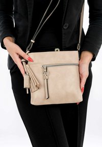 Beige leather crossbody bag with a zippered front pocket, tassel accent, and a detachable shoulder strap, featured against a neutral background.