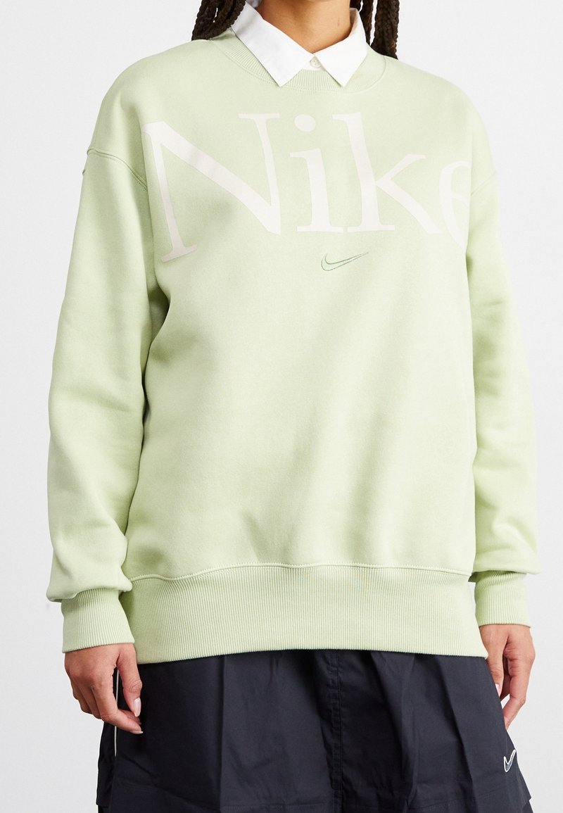 Light green sweatshirt with oversized fit, featuring large "Nike" logo and small swoosh detail. Ribbed cuffs and hem add texture.