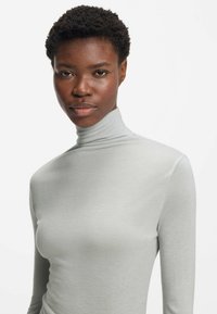 Light gray turtleneck top made of soft, smooth fabric with long sleeves and a fitted silhouette, featuring a high neckline.