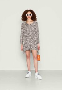 Vestido floral em preto e branco, com mangas longas e decote em V, combinado com ténis brancos e uma bolsa laranja.