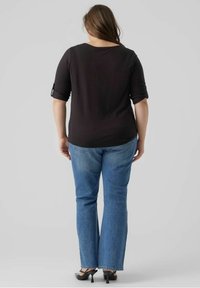 Top nero aderente con maniche a tre quarti. Abbinato a jeans chiari a zampa d'elefante con orli sfilacciati e scarpe con tacco nere.
