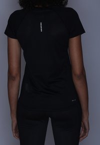 Camiseta atlética negra de manga corta tipo raglán, con un acento reflectante en la parte posterior, hecha de una tela ligera y transpirable.