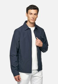 Giacca blu navy con taschino sul petto con bottoni, chiusura zip davanti e colletto classico. Realizzata in un materiale leggero e liscio.