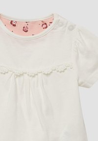 Witte babyshirt met korte mouwen, kantafwerking onder de borst, roze bloemenpatroon aan de binnenkant van de kraag, en twee drukknoopjes op de rechterschouder.