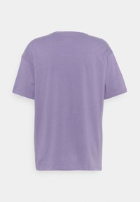 En enkel lavendelfärgad t-shirt med kort ärm sett från ryggen, med rundad halsringning och avslappnad passform mot en vit bakgrund.