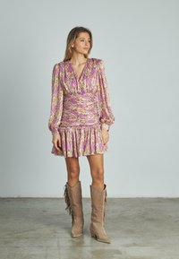 Vestido mini floral con tonos rosas y amarillos, con mangas largas abullonadas y un dobladillo con volantes. Combinado con botas altas de color marrón claro con detalles de flecos.