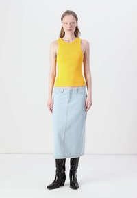 Débardeur jaune côtelé associé à une jupe maxi en denim bleu clair et des bottes noires à la cheville, présentant une texture lisse et une coupe ajustée.