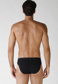 Costumi da bagno neri, con cintura elastica, tessuto liscio e design aderente. La vista posteriore mostra una copertura minima, una costruzione senza cuciture e linee pulite.