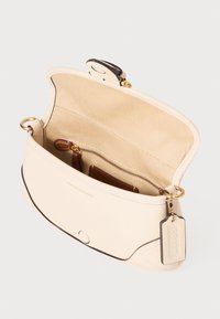Cream leather handbag with curved design, gold hardware, and an interior zip pocket; lined with tan fabric. Features a detachable tag.