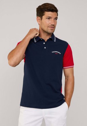Marineblaues Poloshirt mit roten Ärmeln, ausgestattet mit einem knöpfbaren Kragen, weißen Akzenten und gesticktem Logo auf der Brust. Material aus Baumwollmischung.