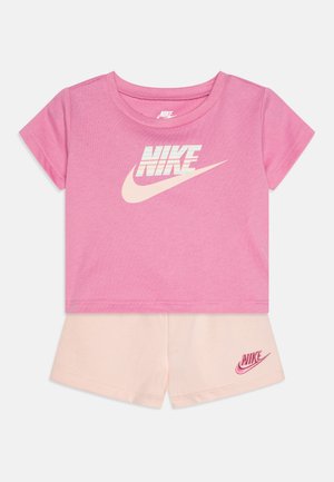 Ροζ βαμβακερό T-shirt με μεγάλο μπεζ λογότυπο Nike και κοντές μπεζ βερμούδες που διαθέτουν μικρό ροζ λογότυπο Nike στο στρίφωμα.