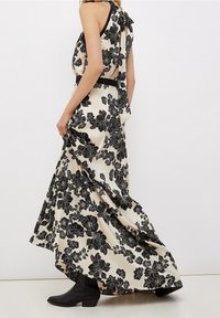 Czarna sukienka maxi w kwiatowy wzór na kremowym tle, z dekoltem halter i kokardą z tyłu, zestawiona z czarnymi botkami za kostkę.