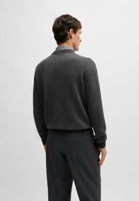 Maglione a coste grigio scuro con un motivo testurizzato e colletto, abbinato a pantaloni scuri coordinati. Design semplice e pulito.