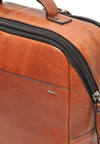 Bruine leren tas met een gladde textuur, voorzien van een zwarte rits, zilveren hardware en een discreet merkembleem aan de zijkant.