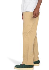 Béžové bavlnené nohavice so strihom rovného nohavca. Obsahujú pútka na opasok a bočné vrecká. Nosia sa so zelenými semišovými teniskami. Jednoduchý a funkčný vzhľad.