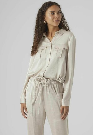 Chemise beige clair à manches longues avec deux poches poitrine, associée à un pantalon à cordon de serrage assorti. Texture lisse avec une coupe décontractée.