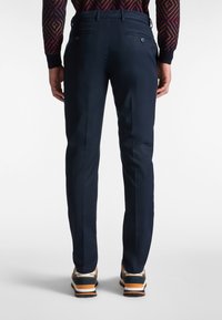 Marinblå byxor med en slim fit, utrustade med två bakfickor med knappar och en smidig textur. Kombineras med sneakers i orangea detaljer.