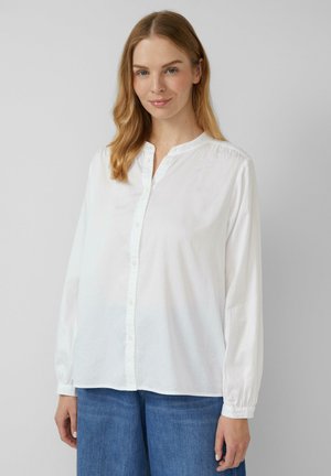 Weißes Langarmhemd mit Knopfleiste, kragenlosem Ausschnitt und Raffung an den Schultern, kombiniert mit blauen Denim-Breite-Hosen.