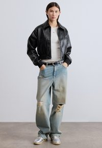 Μαύρο δερμάτινο cropped μπουφάν με γιακά, που φοριέται πάνω από ένα ανοιχτό γκρι πουκάμισο. Ανοιχτό μπλε τζην με σκισίματα και άνετη εφαρμογή. Ασημένια αθλητικά παπούτσια.