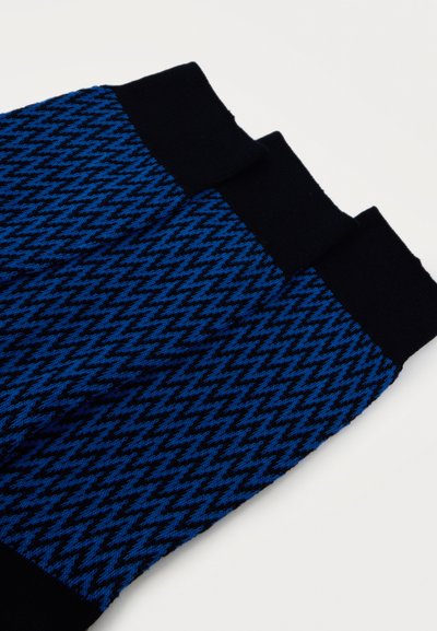 Chaussettes à motif pied-de-poule bleu et noir avec poignets et bouts de pieds noirs unis, posées à plat sur une surface blanche.