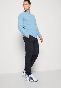 Maglione lavorato a maglia azzurro chiaro con scollatura rotonda, abbinato a pantaloni navy scuri e sneakers bianche con dettagli blu.