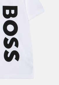 T-shirt blanc en coton, avec l'inscription "BOSS" en lettres noires audacieuses. Manches courtes et ourlet droit avec une texture lisse.