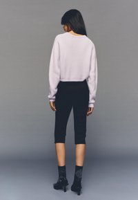 Svetlo sivkasto roza krajši pulover, črne oprijete hlače, vzorčaste nogavice in čevlji z peto. Mehak material z ohlapnim krojem in rebrastimi manšetami.