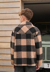 Chaqueta de forro polar en patrón de cuadros en tonos marrón y negro, con cuello tipo solapa, tejido texturizado y corte relajado, vista desde la parte posterior.