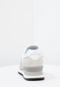 Valkoiset ja harmaat tennarit, joissa on nubukkia ja verkkomateriaaleja, varustettuna pehmustetulla nilkkatuella, logolla kantapäässä ja kuvioidulla kumipohjalla.