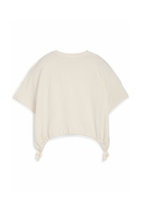 Camiseta corta de color beige claro con mangas caídas, dobladillo ajustado y pequeños flecos a los lados. Fabricada con una tela suave y ligera.
