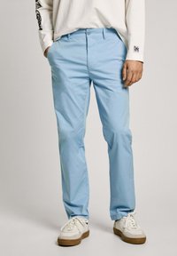 Gaiši zilas kokvilnas bikses ar taisnu kāju dizainu, aprīkotas ar pogu aizdari un kabatām. Apvienotas ar baltām sporta kurpēm.