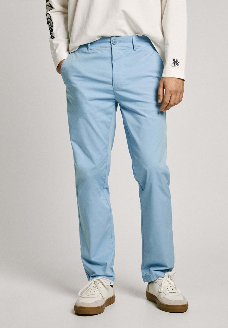 Gaiši zilas kokvilnas bikses ar taisnu kāju dizainu, aprīkotas ar pogu aizdari un kabatām. Apvienotas ar baltām sporta kurpēm.