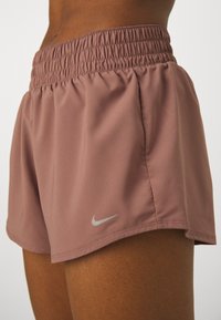 Nike löparshorts i en mjuk mauve-färg, med ett elastiskt midjeband, slät tyg och en liten silverfärgad swoosh-logga på benet.