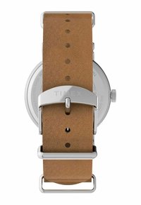 Bracelet en cuir brun avec une boucle en métal argenté, comportant plusieurs encoches. Boîtier rond en acier inoxydable avec un fond transparent et un design simple.
