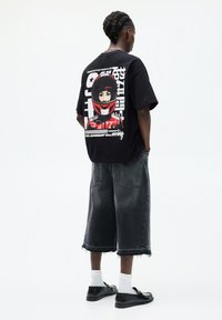 Black oversized t-shirt with graphic print of a helmeted figure on the back. Paired with loose, gray denim shorts and black shoes.
