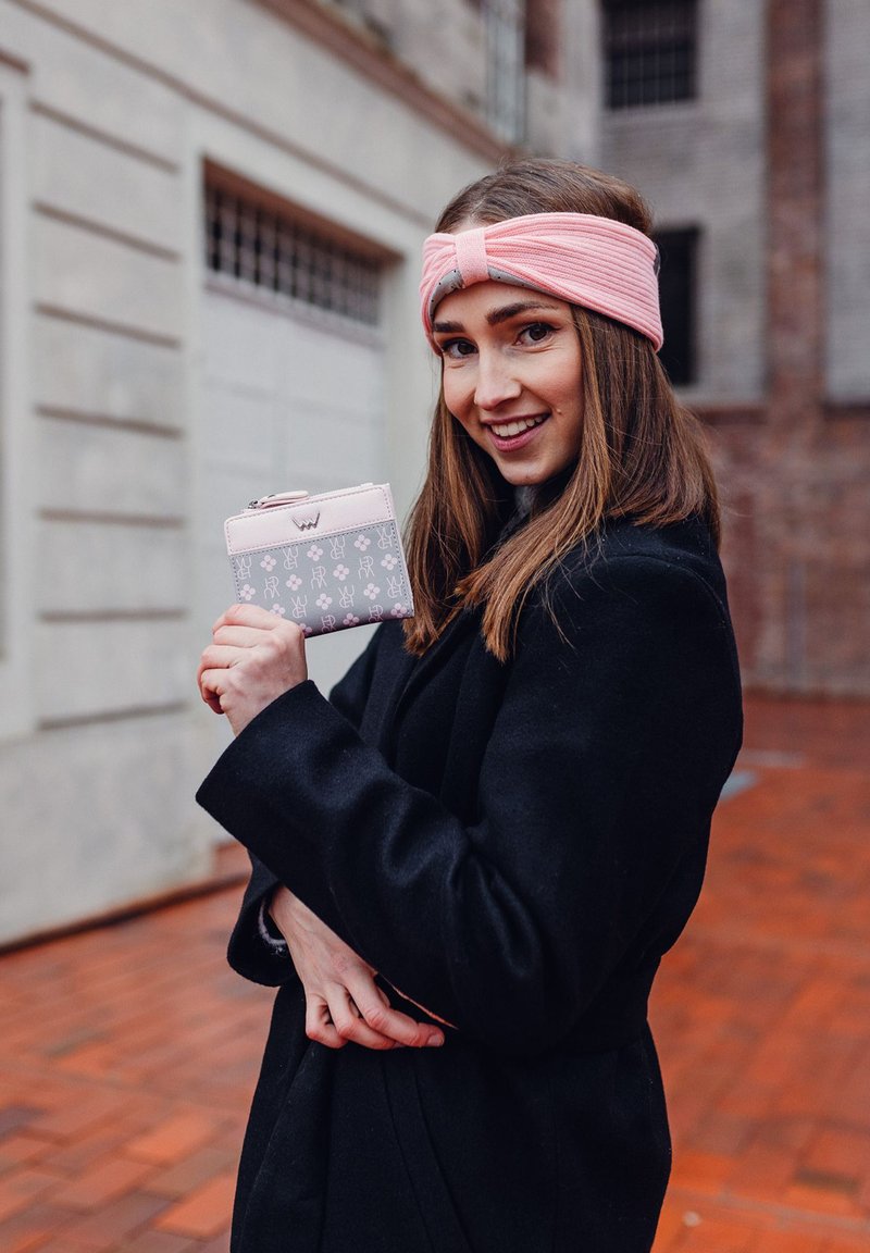 Peneženka na zip v šedé barvě s růžovými akcenty a vzory králíčků. Měkký růžový čelenka, černý kabát a pozadí z dřevěné podlahy.