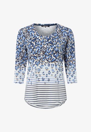 Blaue und weiße Bluse mit Dreiviertelärmel, die ein Leopardenmuster aufweist, das sich am unteren Ende in horizontale Streifen verwandelt.