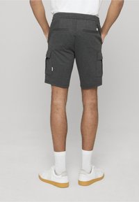 Shorts cargo gris charbon avec poches, taille élastique et coupe décontractée. Portés avec des baskets blanches et des chaussettes. Vue de dos.