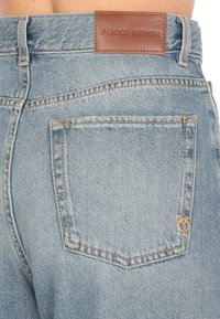 Vaqueros de mezclilla azul claro con un parche de cuero en la cintura etiquetado "PINKO DENIM", que presentan bolsillos traseros estándar y costuras en contraste.