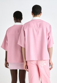 Rózsaszín, rövid ujjú felsők diszkrét kockás mintával és fehér gallérral, párosítva hozzájuk illő rózsaszín alsó részekkel, melyek bonyolult virágmintával hímzettek.