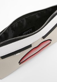 Pestrá kabelka typu clutch v černé, bílé a béžové strukturované kůži, zdobená grafikou červených rtů a se zipovým uzávěrem. Podšívka uvnitř.