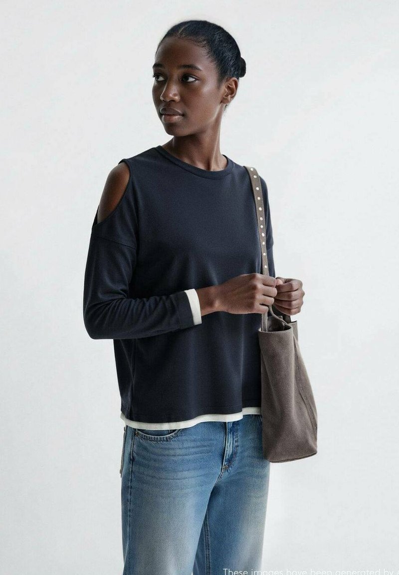 Navy long-sleeve top with shoulder cut-outs, white accents at the hem, paired with light blue jeans and a gray bag with a shoulder strap.