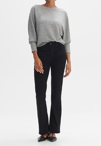 Maglione grigio a maniche lunghe, oversize, con polsini a coste, abbinato a jeans neri a gamba dritta e ballerine nere. Design semplice, texture liscia.